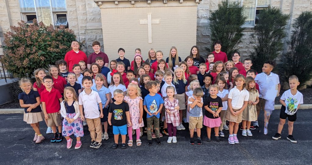 Students of St. Joseph Catholic School gathered outside in front of the church, smiling together as a school community.
